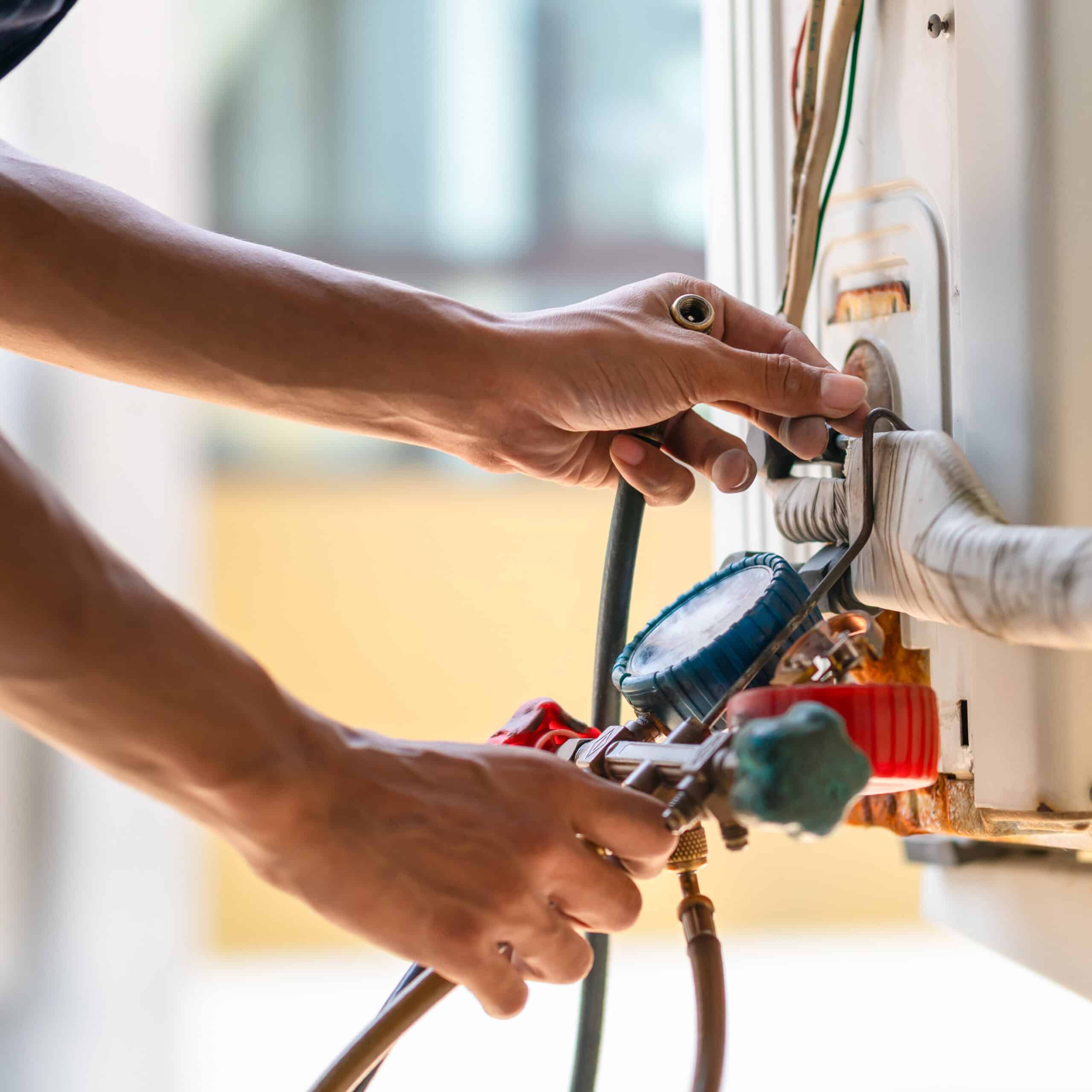 Mains d'un technicien réparant une unité de climatisation extérieure, utilisant un manomètre pour l'entretien et la recharge de fluide.