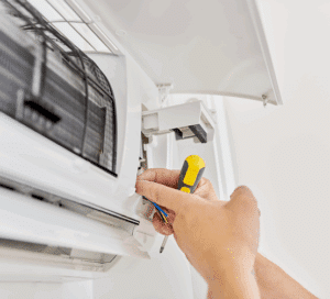 Mains d'un technicien réparant un climatiseur mural blanc avec un tournevis. Maintenance et nettoyage de l'unité intérieure.